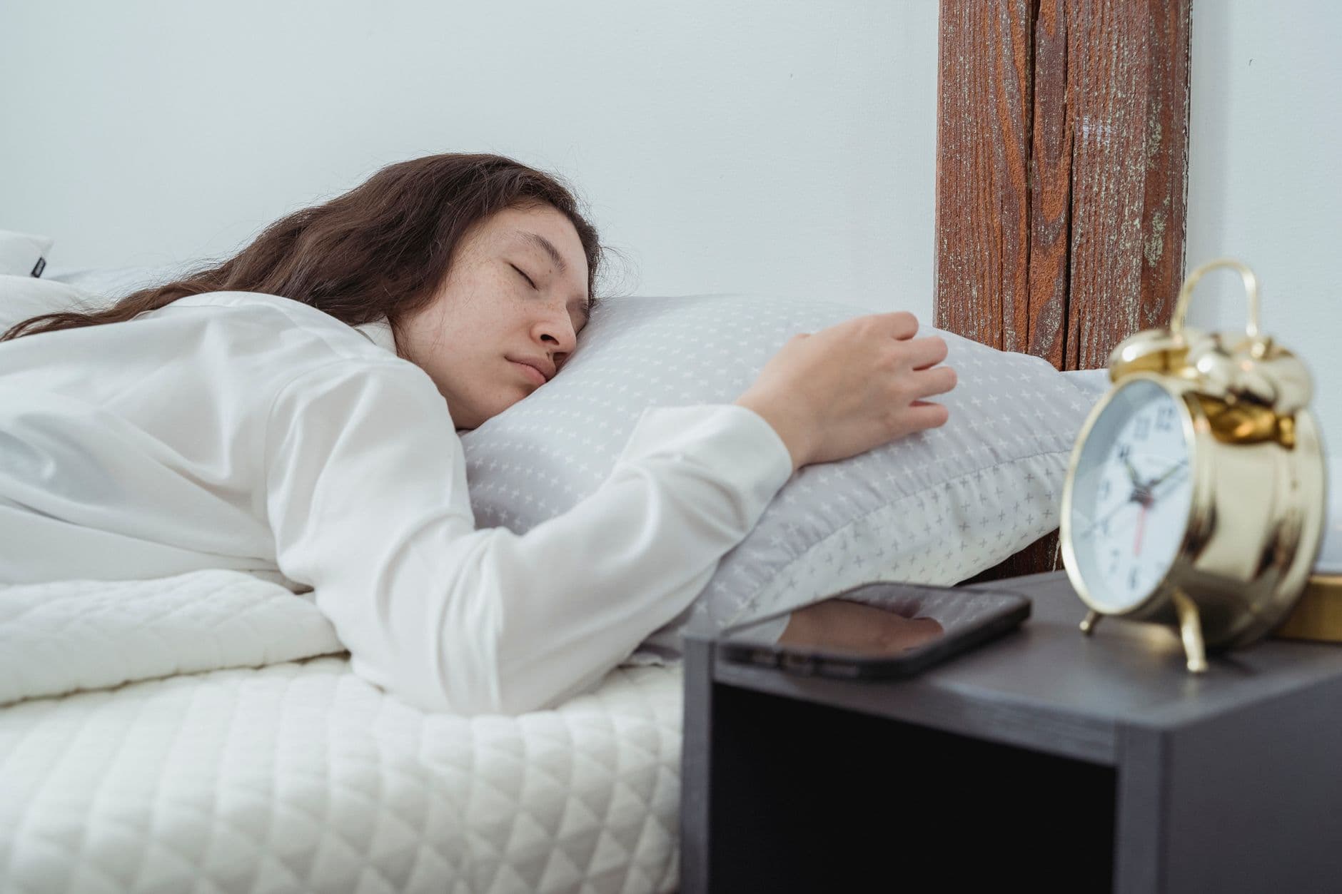 A hand reaching to silence a phone alarm in bed