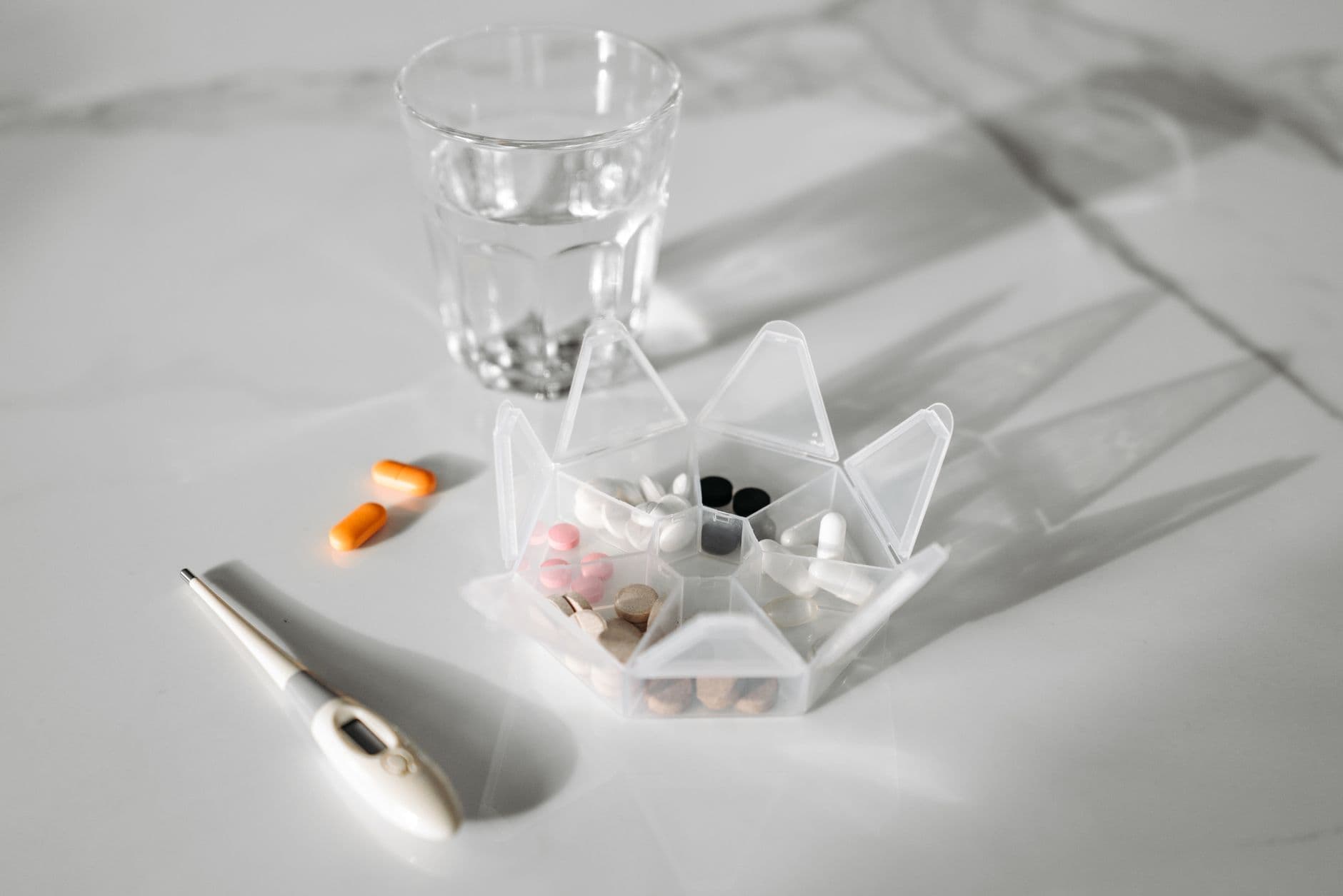 A weekly pill organiser beside a glass of water