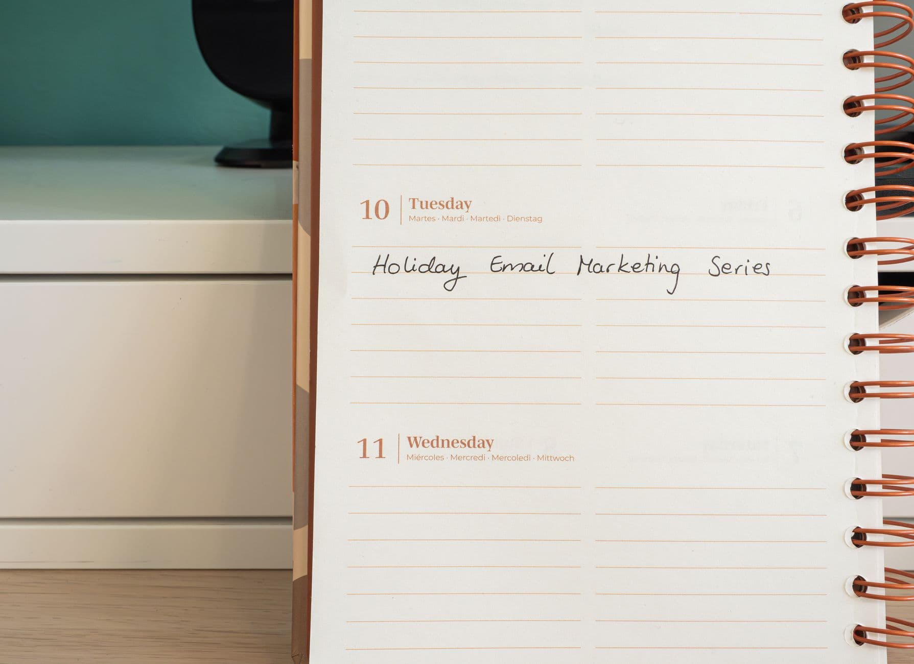 Someone planning a week of work in a notebook beside a laptop