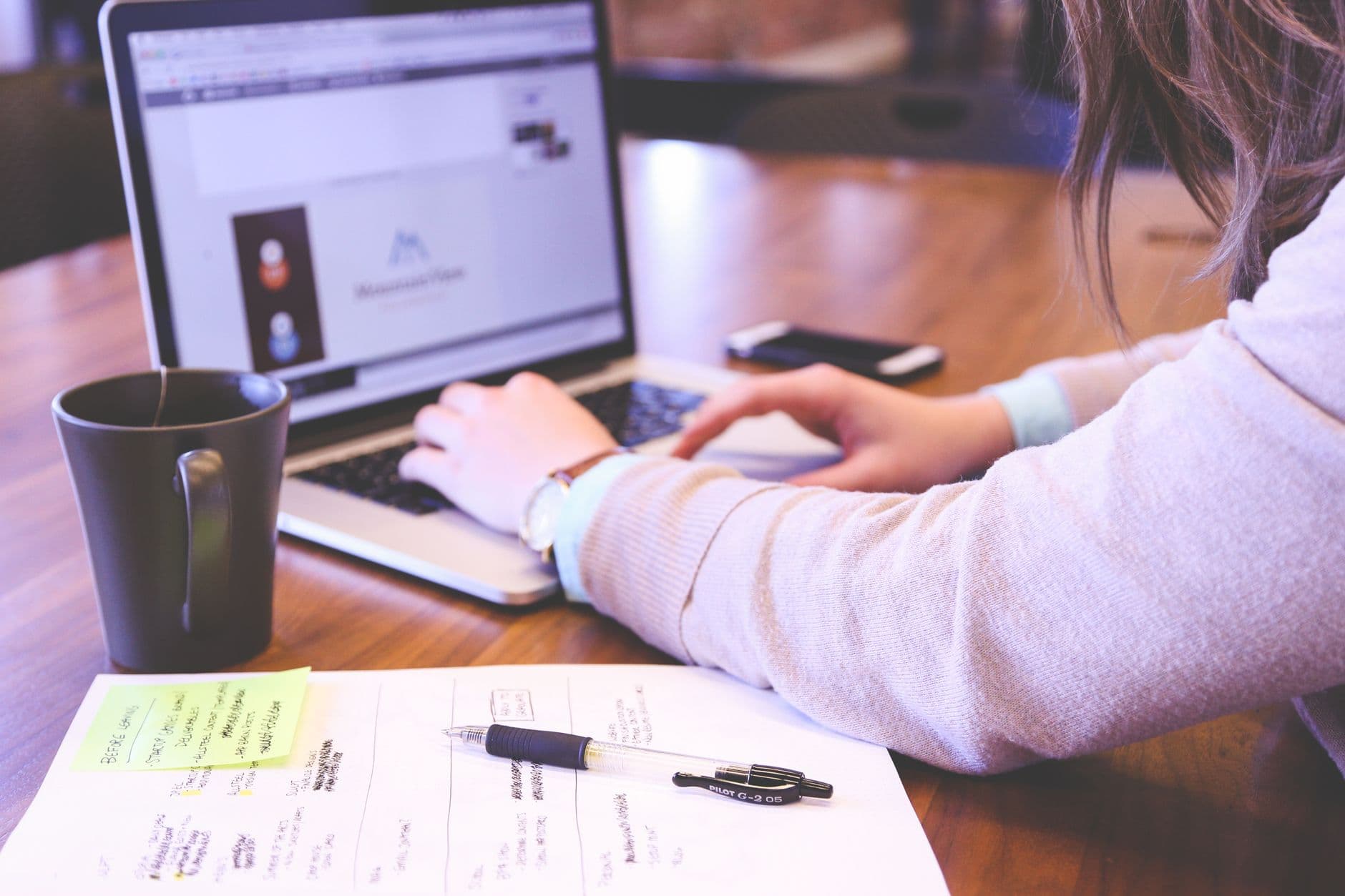 A laptop showing a notes document beside a coffee cup on a desk