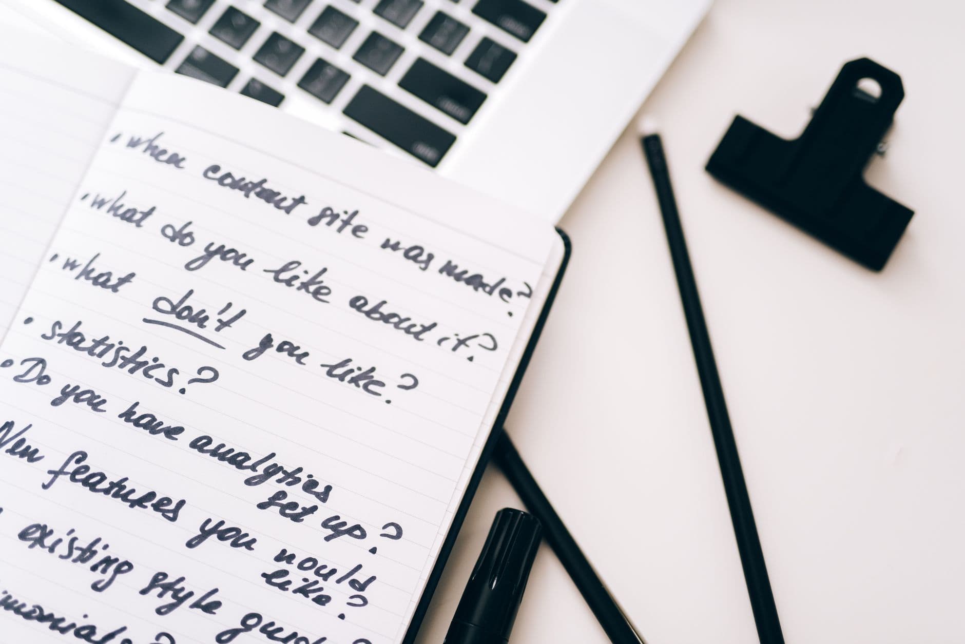 A notebook of handwritten interview questions next to a laptop
