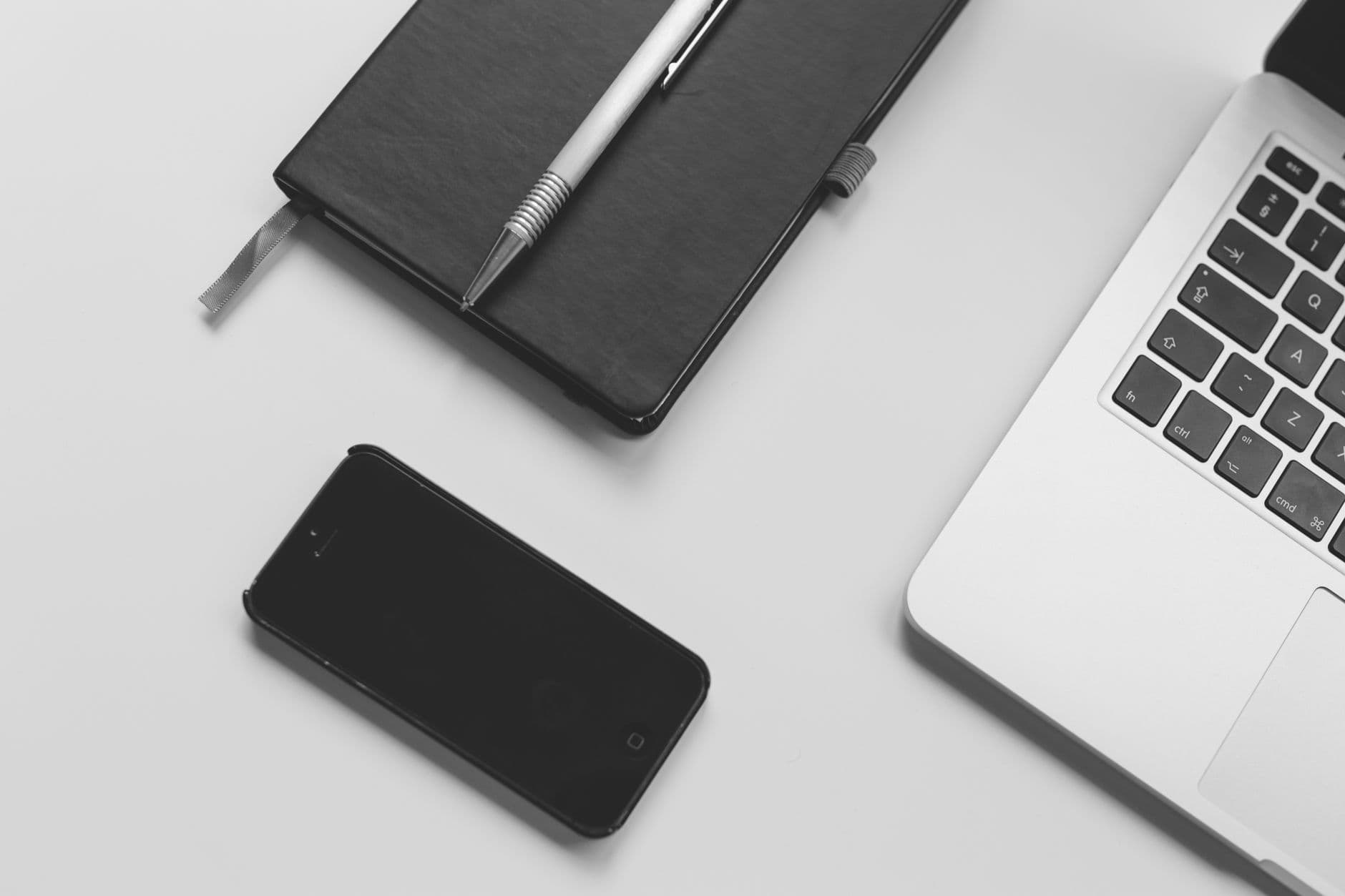 A laptop and smartphone side by side on a desk with a notebook