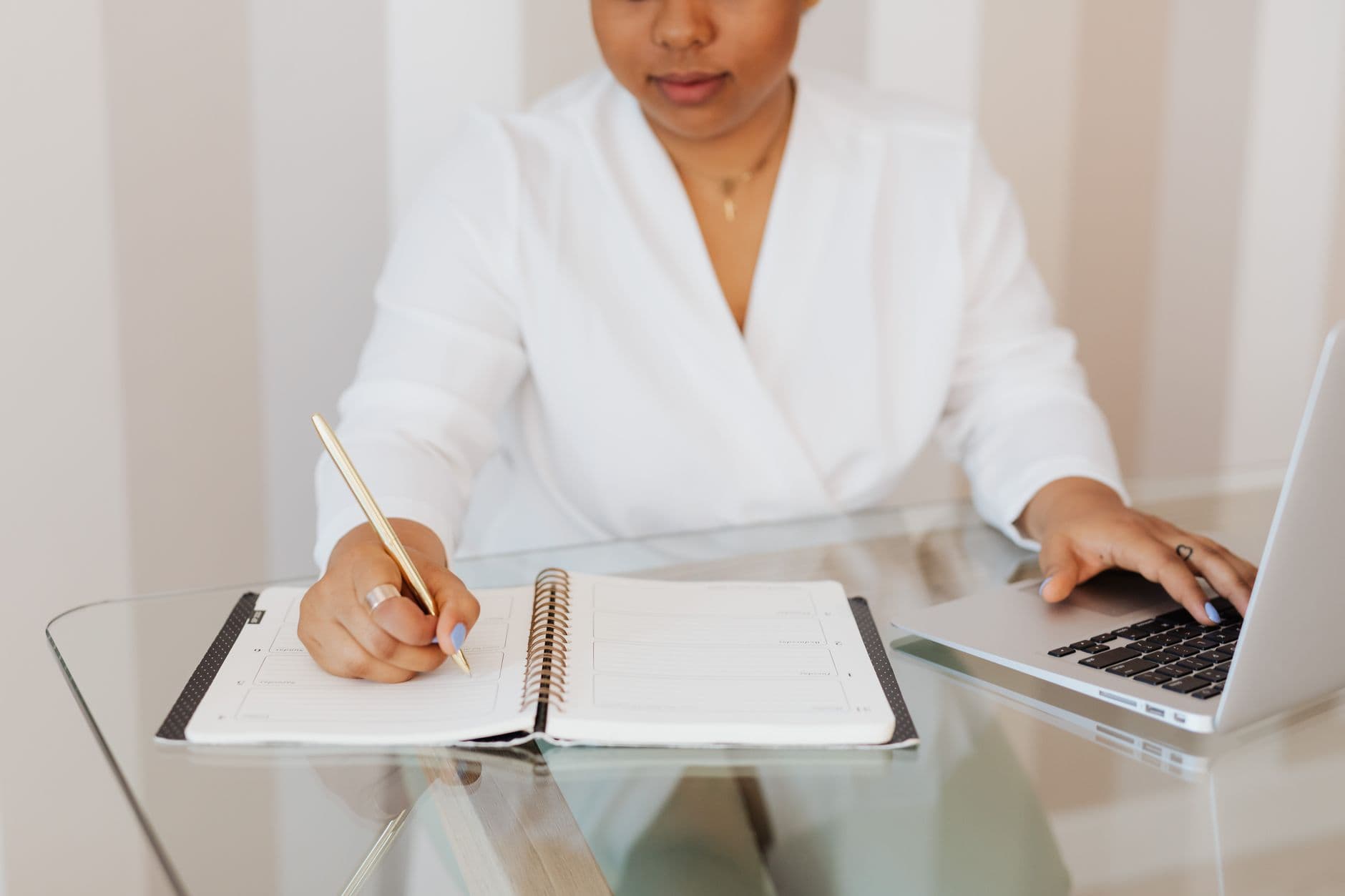 A woman planning her weekly schedule on a laptop next to a notebook